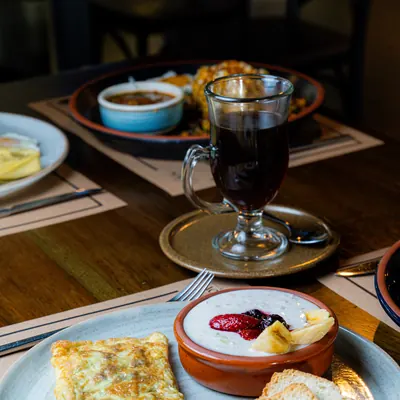 Copa de vidrio con café caliente humeante junto a un omelette con pan tostado y un yogur con frutas