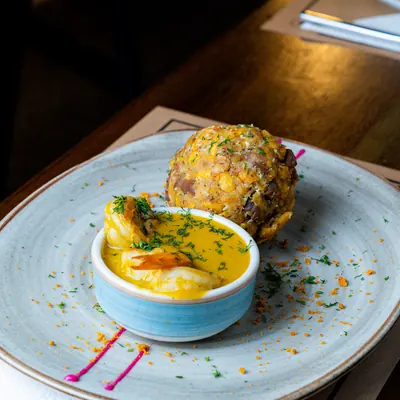 Bolón de verde con chicharrón junto a un bowl de salsa de queso con camarón, con la salsa pintada en el plato