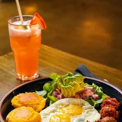 Desayuno de tortillas de maduro con huevos fritos, chorizo y ensalada con aguacate en plato negro