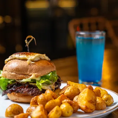 Hamburguesa con queso y lechuga acompañada de papas baby doradas y un vaso de bebida azul