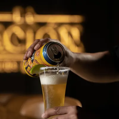 Copa alta de cerveza dorada con espuma sobre la barra, con el rotulo iluminado de La Nacion al fondo.